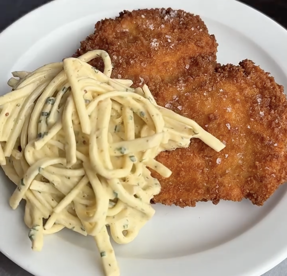 Crispy schnitzel with creamy herb spaghetti on a white plate
